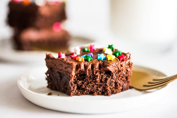 Photograph of frosted brownie with a bite out of it on a white plate.