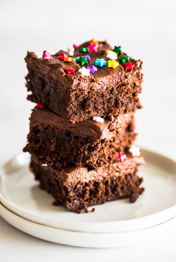 Picture of three frosted brownies stacked on a white plate.