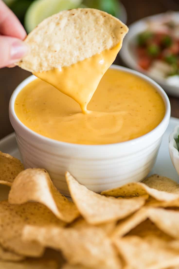 Picture of tortilla chip being dipped into homemade nacho cheese.