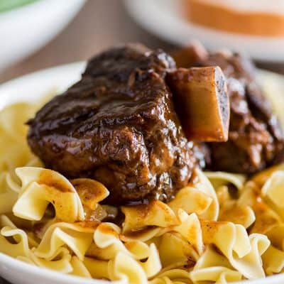Photo of braised short ribs over egg noodles in a white bowl.