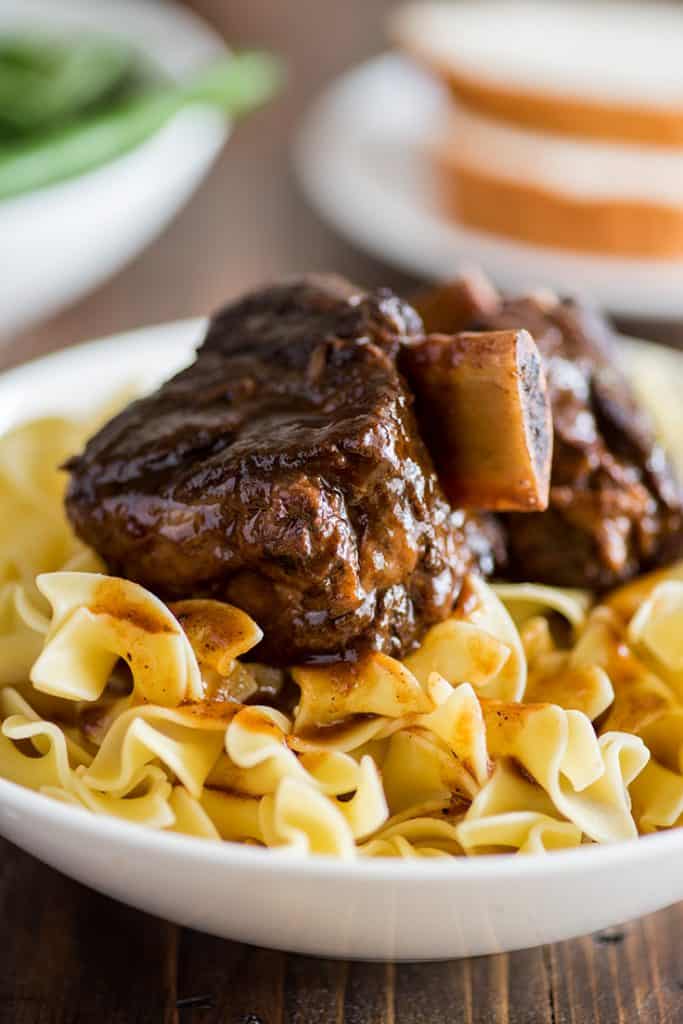 Photo of braised short ribs over egg noodles in a white bowl.