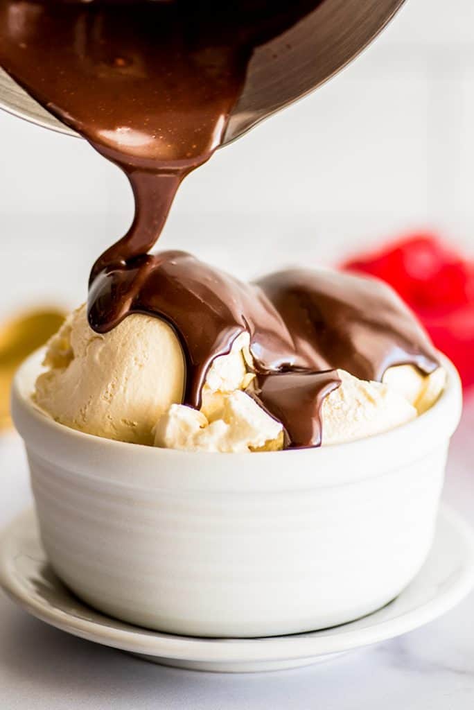 Photo of hot fudge sauce for one being drizzled over ice cream in a white bowl.