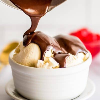 Photo of hot fudge sauce for one being drizzled over ice cream in a white bowl.