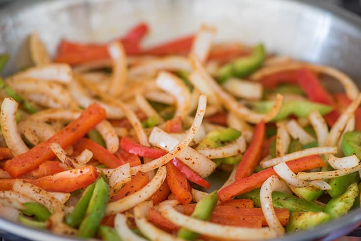Onions and red and green bell peppers in a skillet for fajitas.