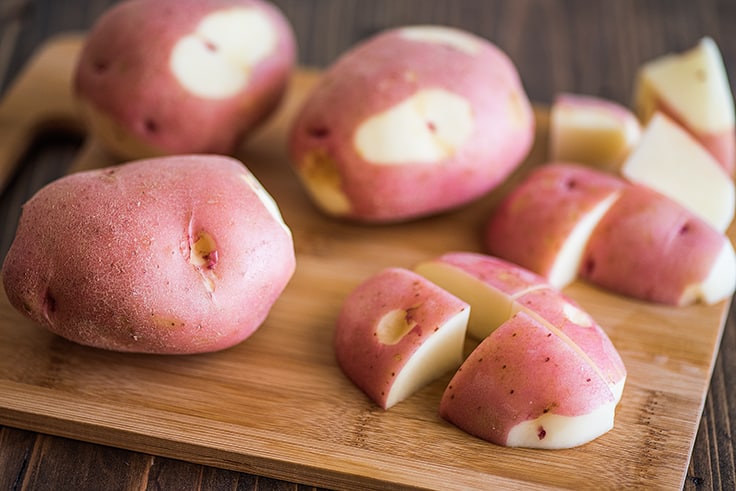 Red potatoes being cut on a cutting board.