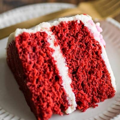 Photo of Small Red Velvet Cake slice on a white plate with gold fork.