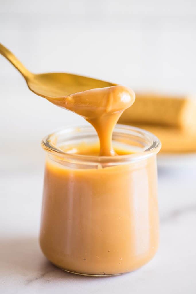 Photo of homemade dulce de leche being spooned out of a jar.