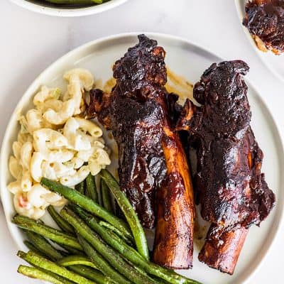 Beef ribs on a plate with pasta salad and green beans.