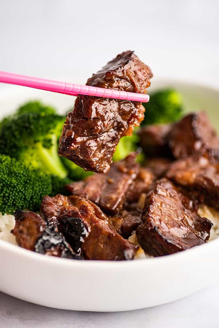 A piece of Beef Teriyaki being held by chopsticks.