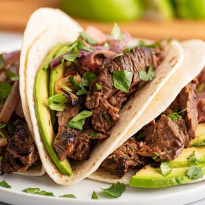 Three carne asada tacos with avocado on a plate.
