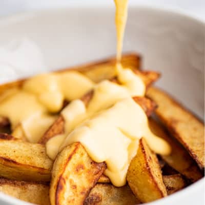 Cheese sauce being poured over fries.