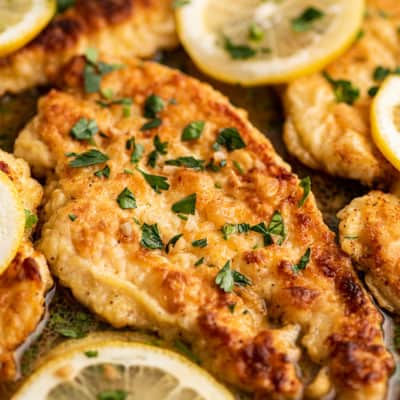 Chicken Francaise in a pan with lemon slices.