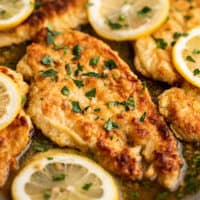 Chicken Francaise in a pan with lemon slices.