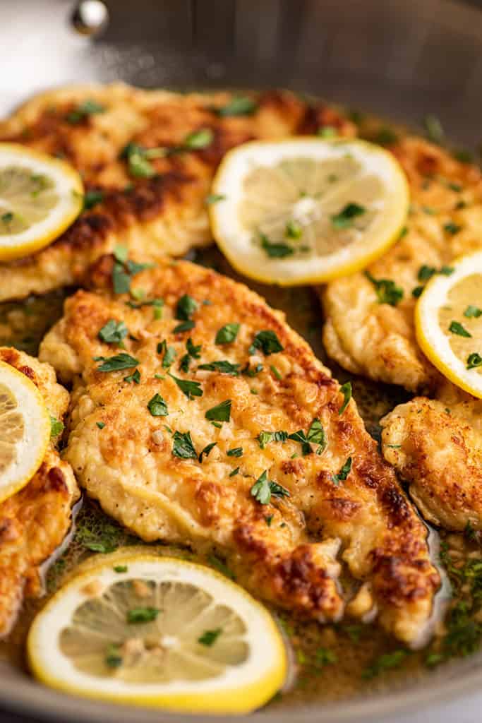Chicken Francaise in a pan with lemon slices.
