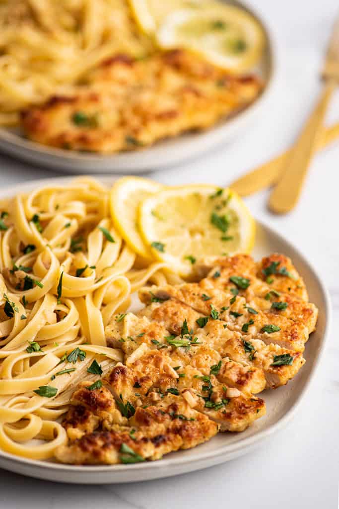 Sliced Chicken Francaise on a plate with fettuccine.