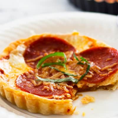 Pizza tart on a white plate with a bite out of it.