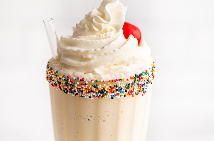 Vanilla milkshake with whipped cream and cherry in a glass cup.