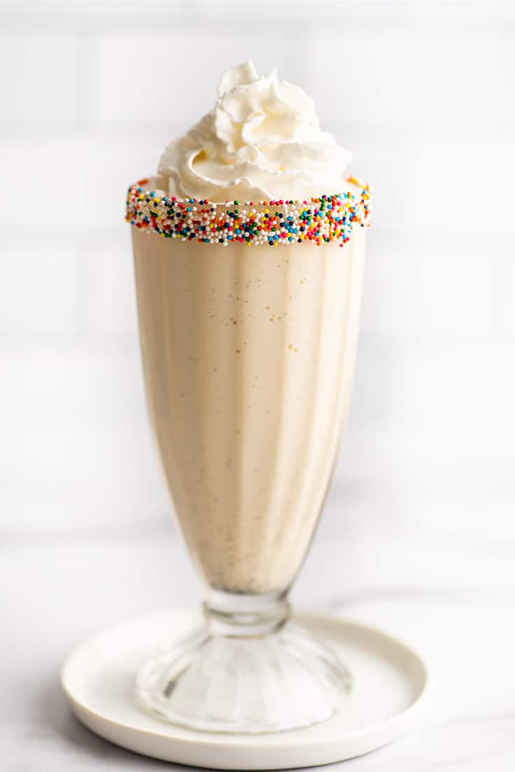 Vanilla milkshake in a glass cup with sprinkles around the rim.
