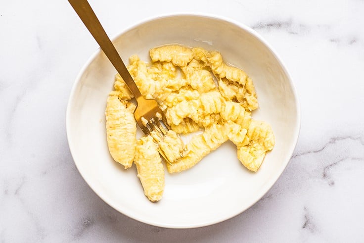Oven-ripened bananas being mashed in a bowl.