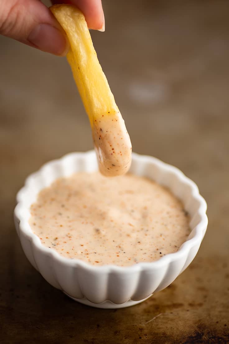 A fry being dipped into chipotle aioli.
