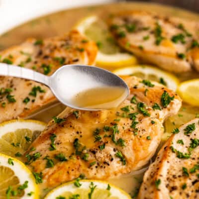 Spooning white wine lemon butter sauce over chicken breast in a skillet.