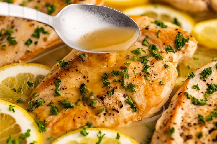 Spooning white wine lemon butter sauce over chicken breast in a skillet.