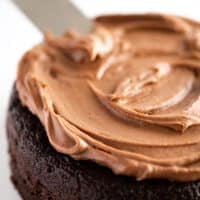 Chocolate cake being frosted with a small batch of chocolate cream cheese frosting.