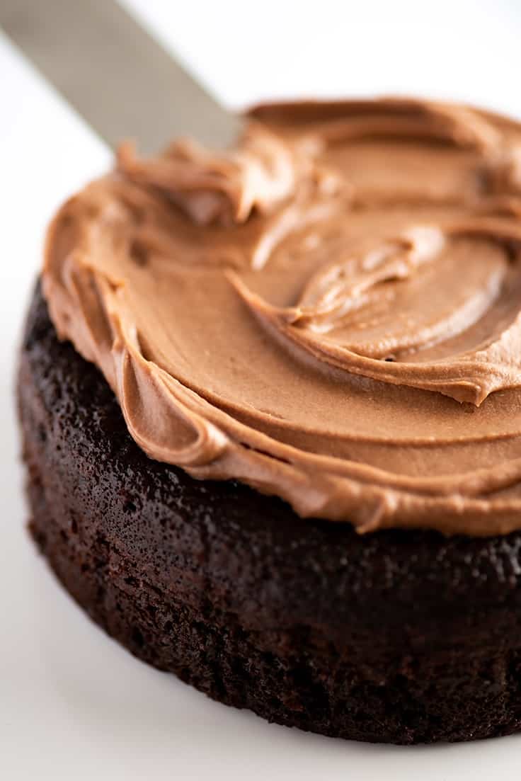 Chocolate cake being frosted with a small batch of chocolate cream cheese frosting.