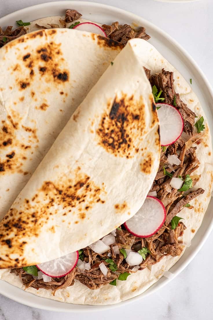 Barbacoa tacos on a white plate.