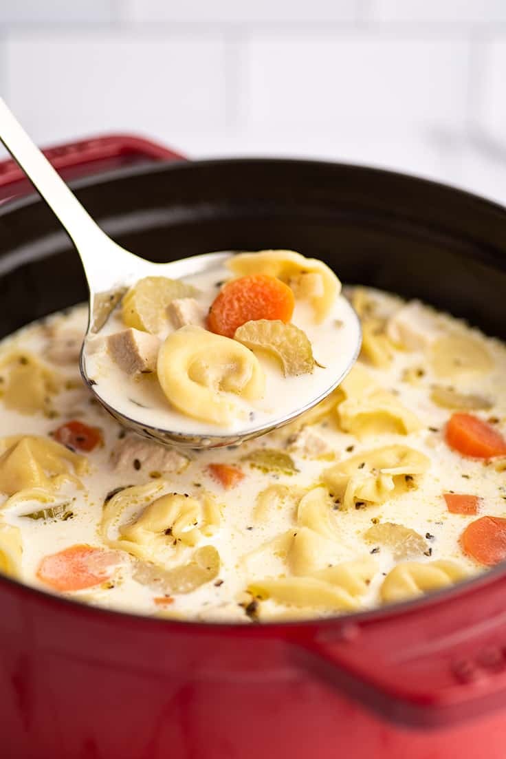 Chicken tortellini soup being ladled out of a red pot.