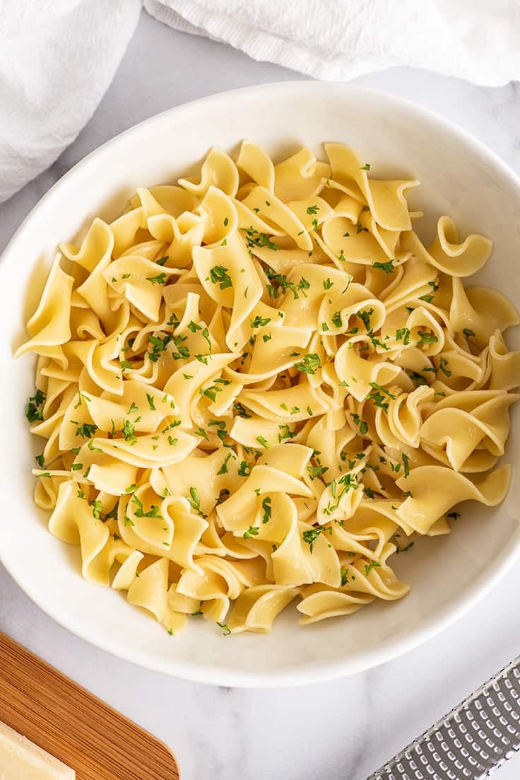 Overhead photo of buttered noodles in a white bowl.