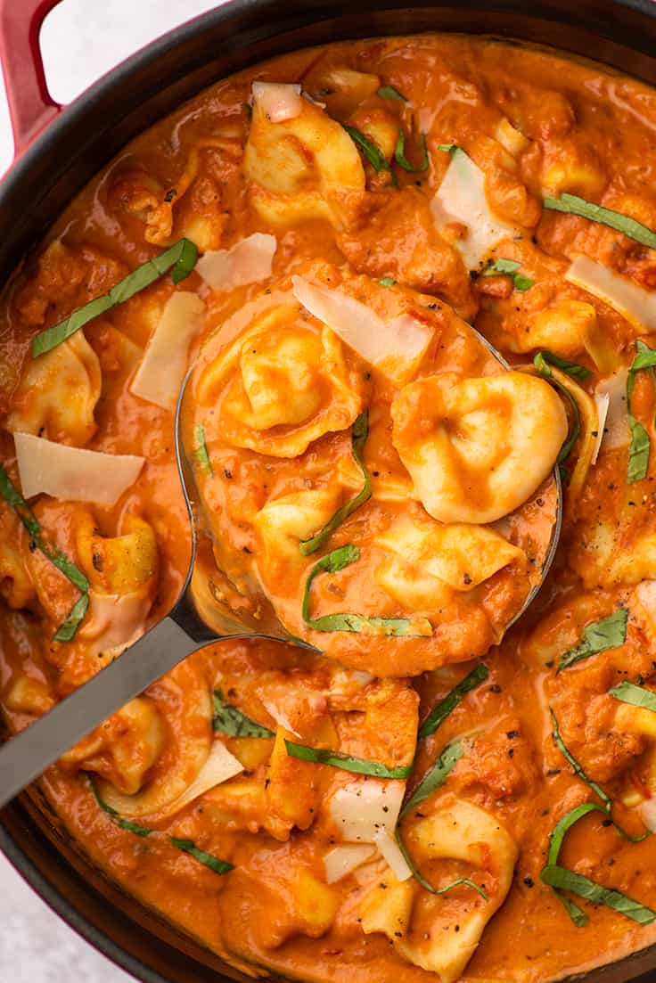 Tomato tortellini soup being ladled out of a pot.