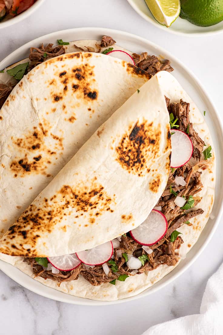 Barbacoa tacos on a white plate.