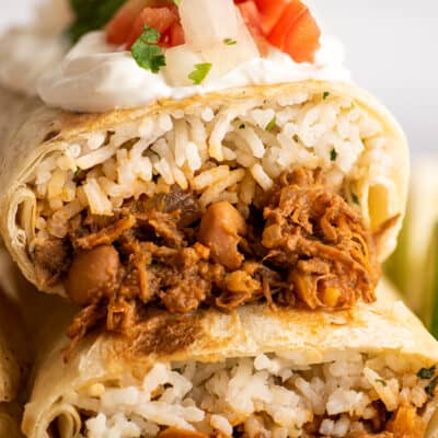 Close up photo of shredded beef burritos stacked.