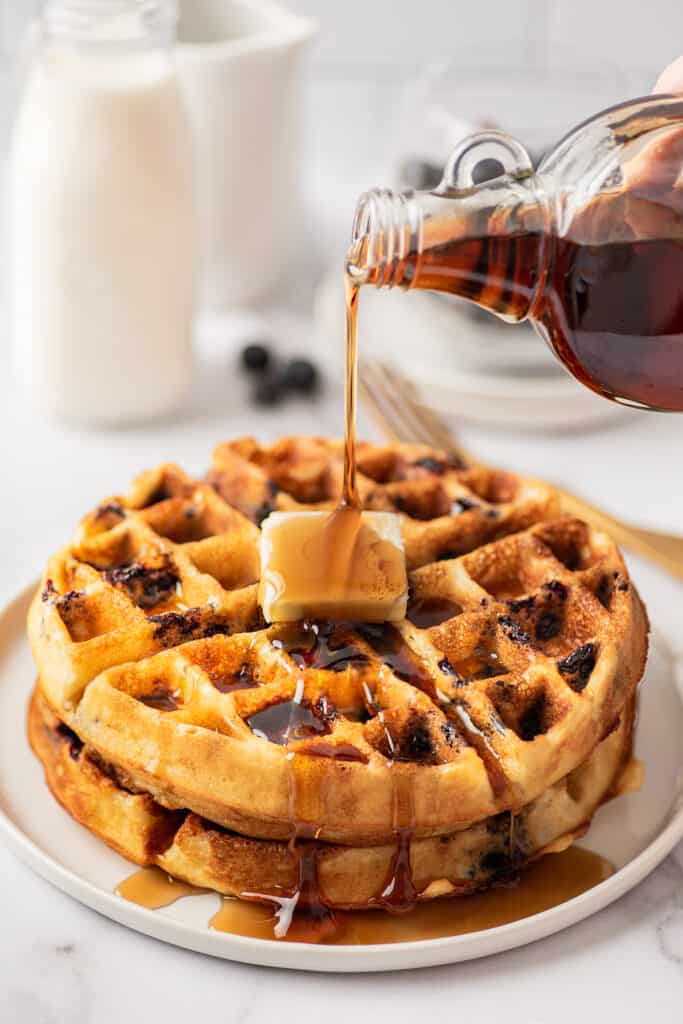 Syrup being poured over blueberry waffles.