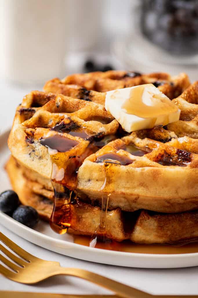 Blueberry waffles stacked on a plate with butter and syrup.