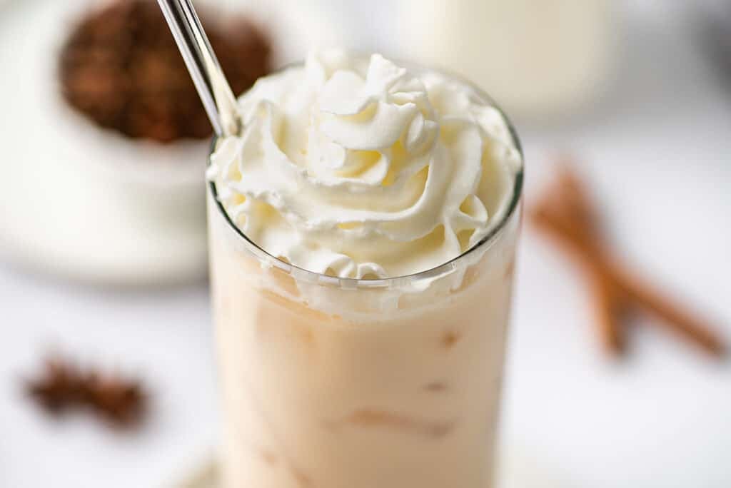 Close photo of iced chai latte with whipped cream on top.