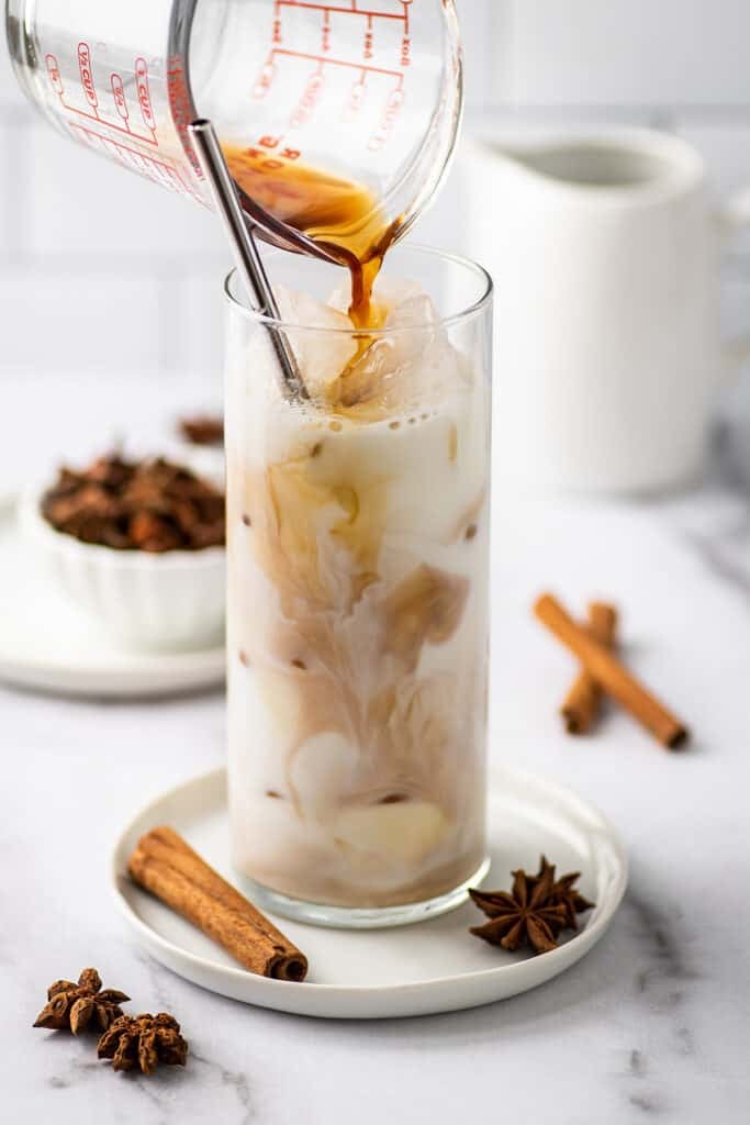 Chai concentrate being poured into milk for a chai latte.