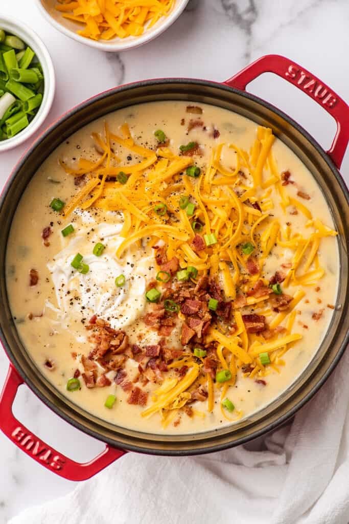 Potato bacon soup topped with cheese, bacon, and sour cream in a pot.