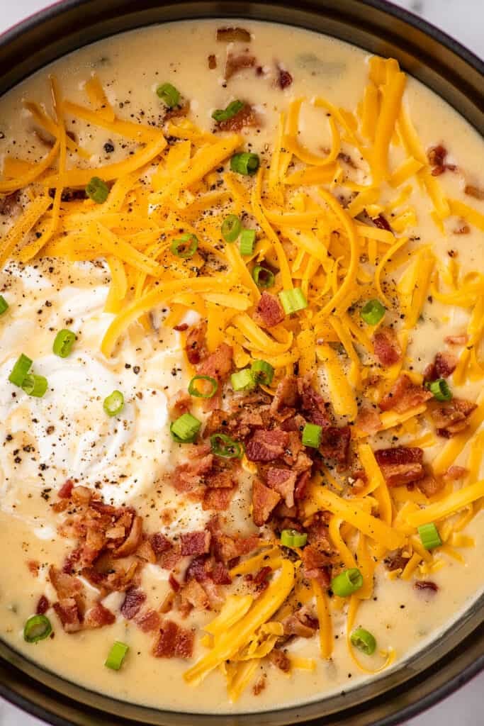 Close photo of potato bacon soup topped with cheese, bacon, and sour cream in a pot.