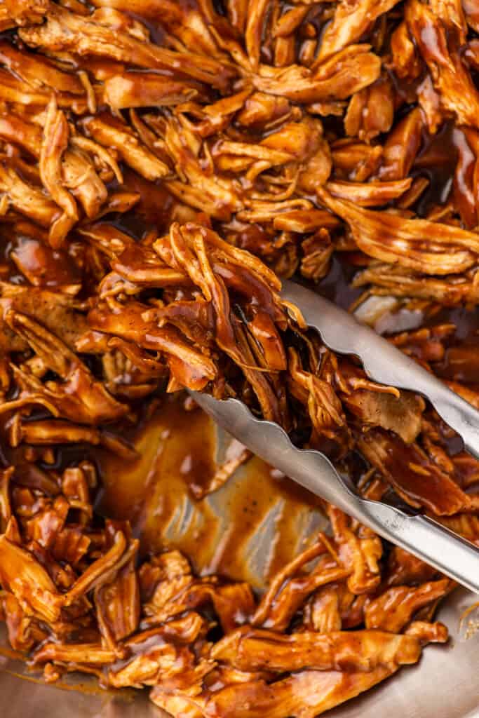 BBQ shredded chicken being picked up with tongs.