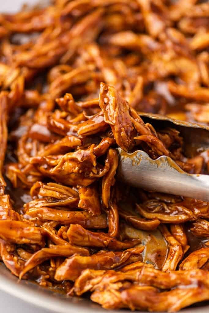 BBQ shredded chicken being picked up with tongs.