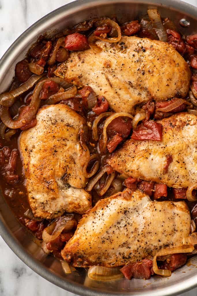 Close up photo of balsamic chicken in a skillet with tomatoes and onions.