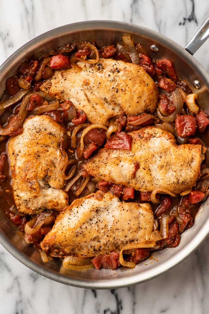 Balsamic chicken in a skillet with tomatoes and onions.