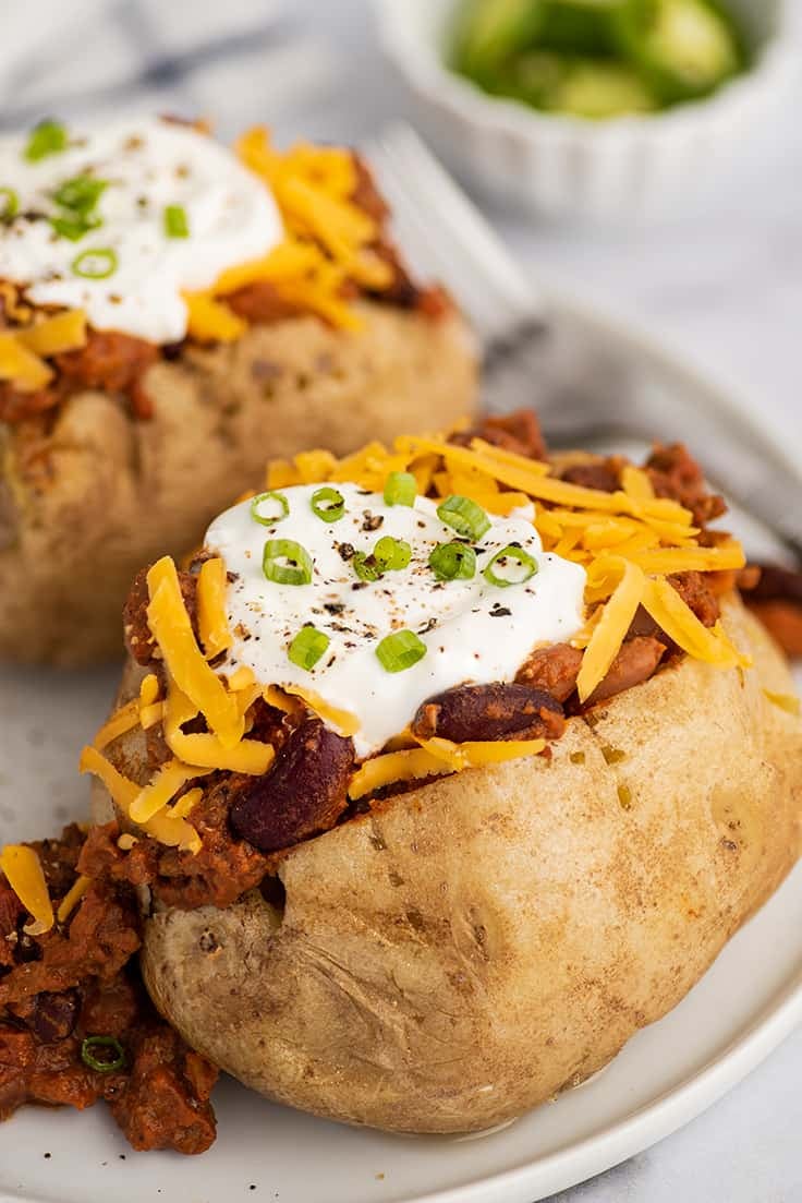 Baked potatoes topped with chili and cheese on a white plate.