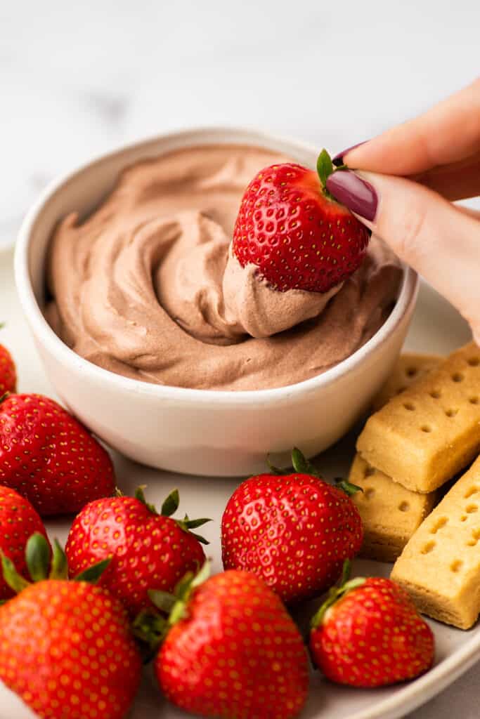Strawberry being dipped into chocolate whipped cream.