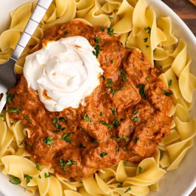 Overhead photo of Hungarian Goulash in a bowl over egg noodles with sour cream.