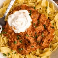 Overhead photo of Hungarian Goulash in a bowl over egg noodles with sour cream.