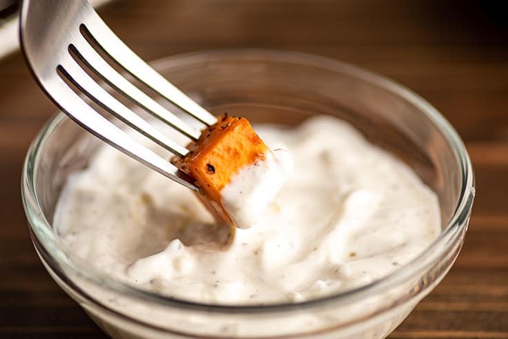 Roasted sweet potato chunk being dipped in aioli.