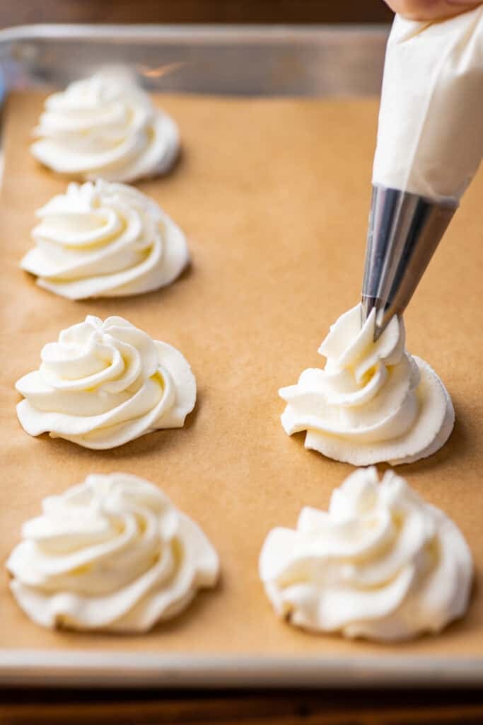 Whipped cream being piped onto a baking sheet for freezing.